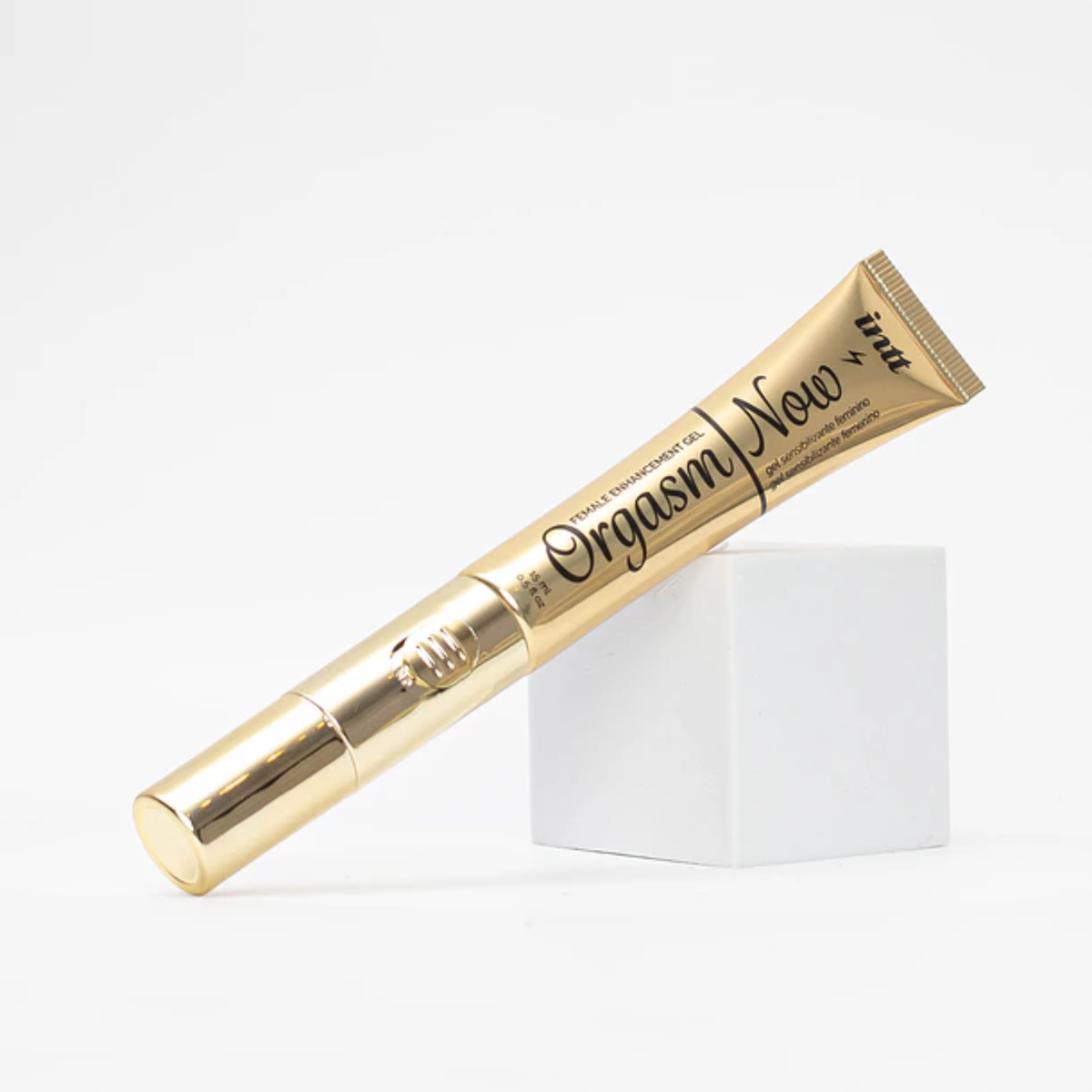 A 0.5 fl oz gold tube of Intt Orgasm Now female arousal gel resting diagonally across a small, white geometric cube prop on a clean white background.