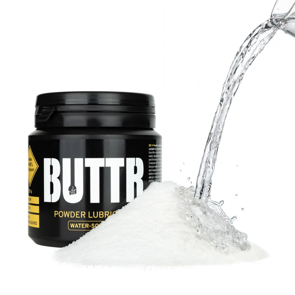 Creative product shot showing water being poured onto a mound of white powder in front of the black BUTTR Powder Lubricant tub.
