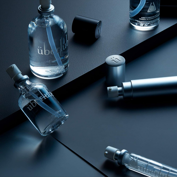 
Various Überlube bottles, some with caps off and a few scattered caps, are elegantly arranged on a dark, reflective surface, creating a sophisticated display. This collection of premium lubricants showcases the sleek design and quality products available through WorldCondoms.