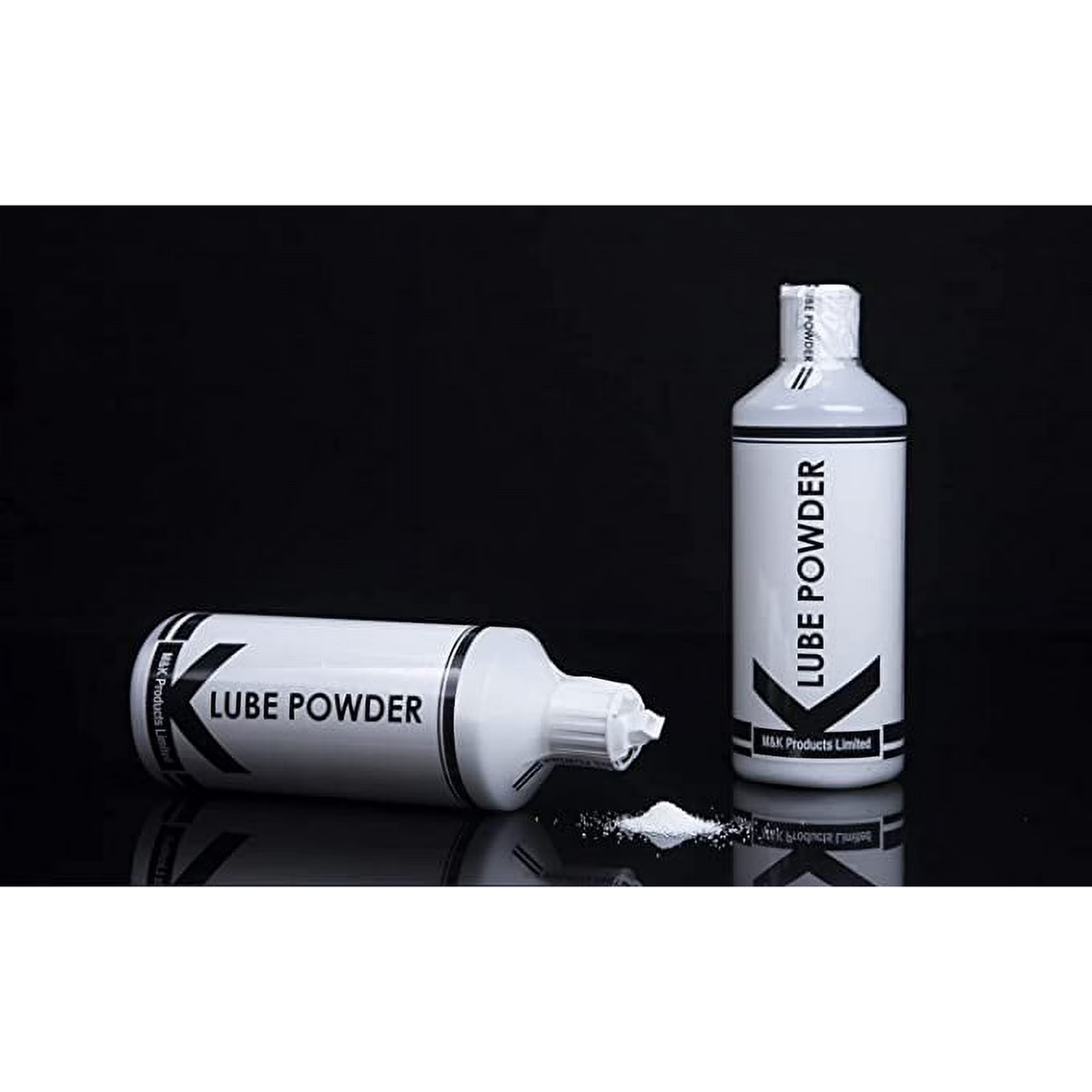 Two bottles of K-Lube Powder shown against a solid black background. One bottle stands upright, while the second bottle lies on its side with the cap open, showing a small pile of the fine white powder spilled onto the reflective black surface.