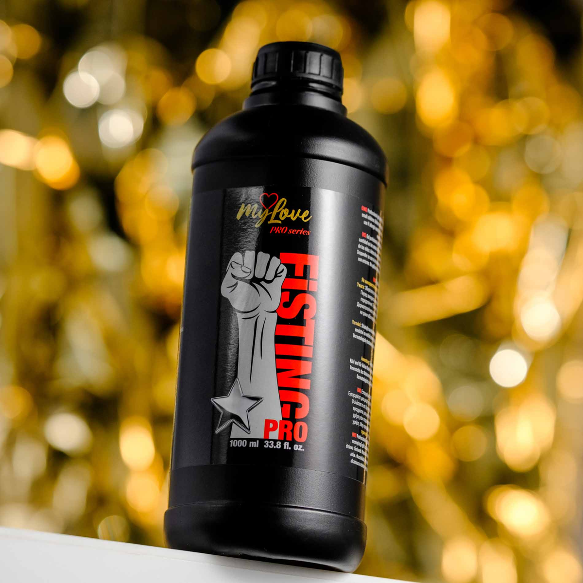 Front view of the 1000 ml MyLove Fisting Pro Gel bottle set against a warm, heavily blurred golden bokeh light background.