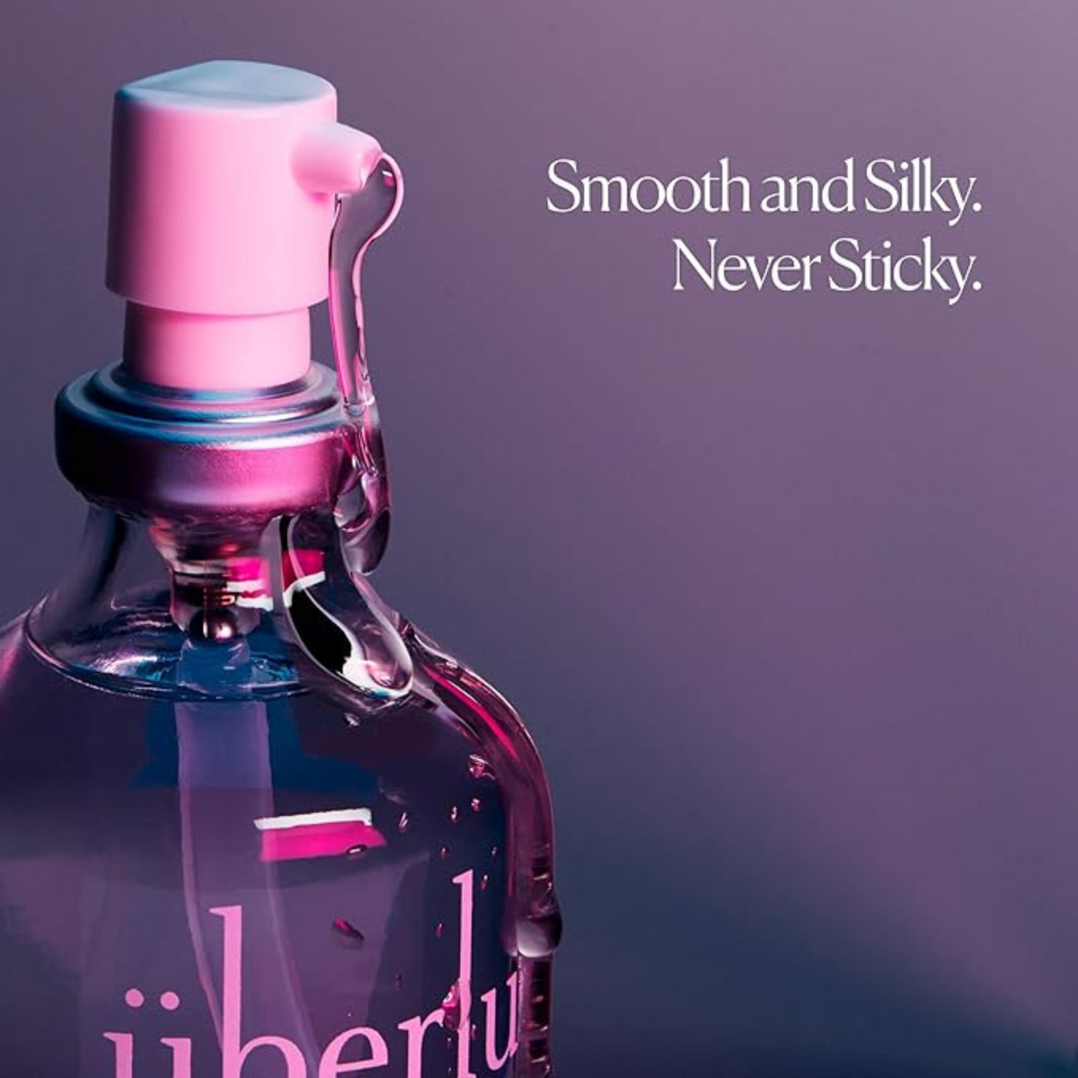 A close-up shot focuses on the top of an Überlube bottle, featuring a vibrant pink pump and visible liquid droplets, against a soft purple background. The prominent text "Smooth and Silky. Never Sticky." highlights the key benefits of this premium lubricant, available through WorldCondoms.