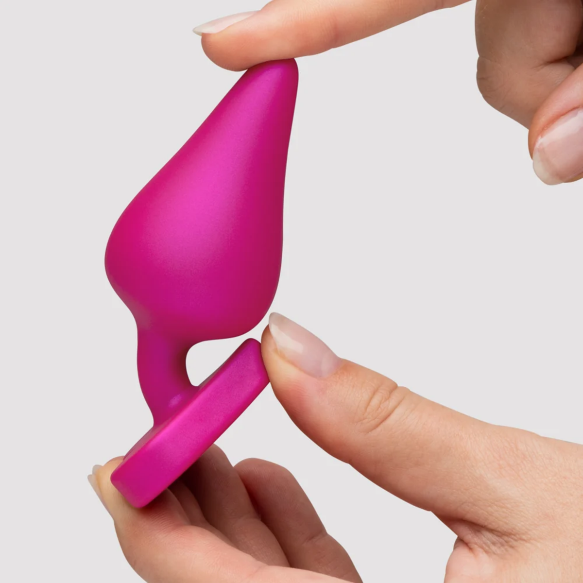 Scale perspective photo showing fingers squeezing the medium-sized pink silicone butt plug to demonstrate its soft, flexible material.