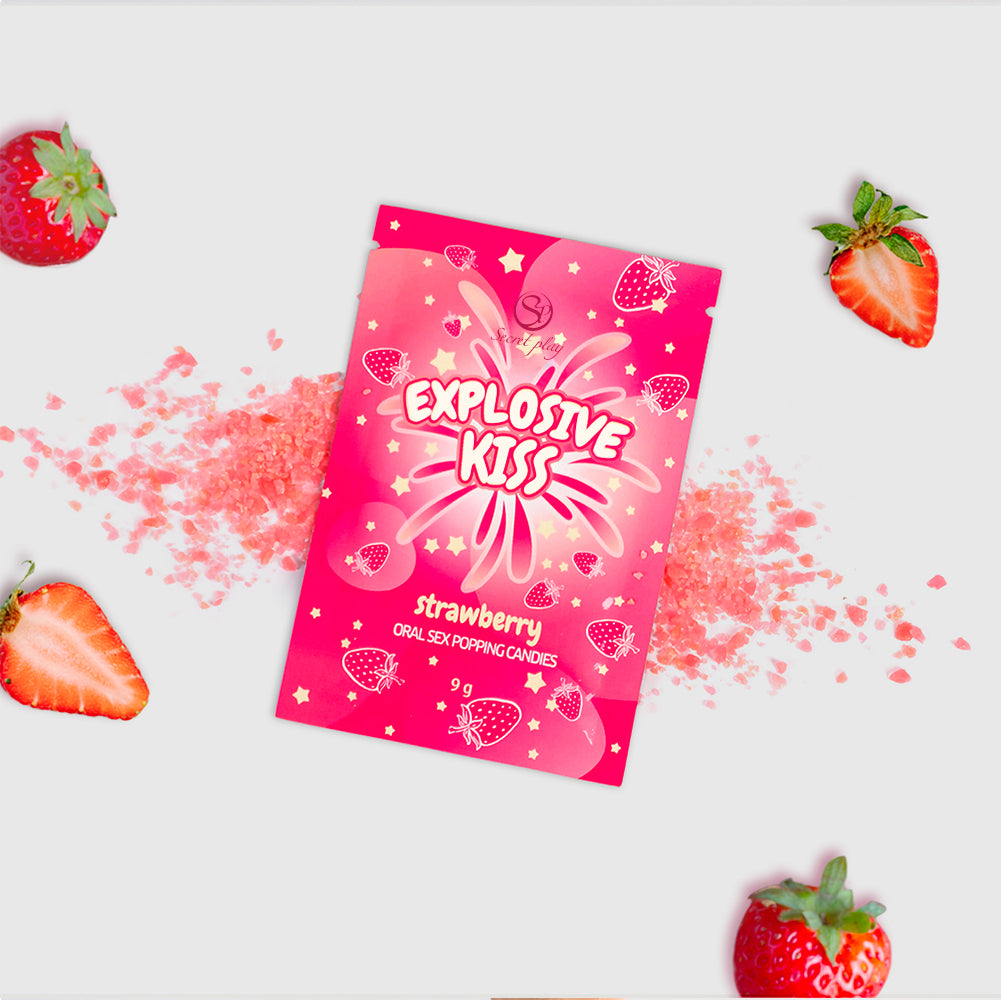 Pink packaging of 'Explosive Kiss' strawberry-flavored product with scattered pink powder and strawberries on a white background.