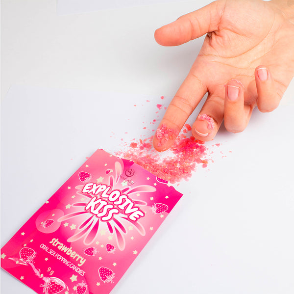 Pink packaging of 'Explosive Kiss' candy with a hand sprinkling pink powder on a white background