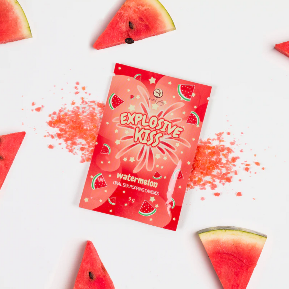 Red packaging of 'Explosive Kiss' watermelon-flavored product with scattered red powder and watermelon bites on a white background.