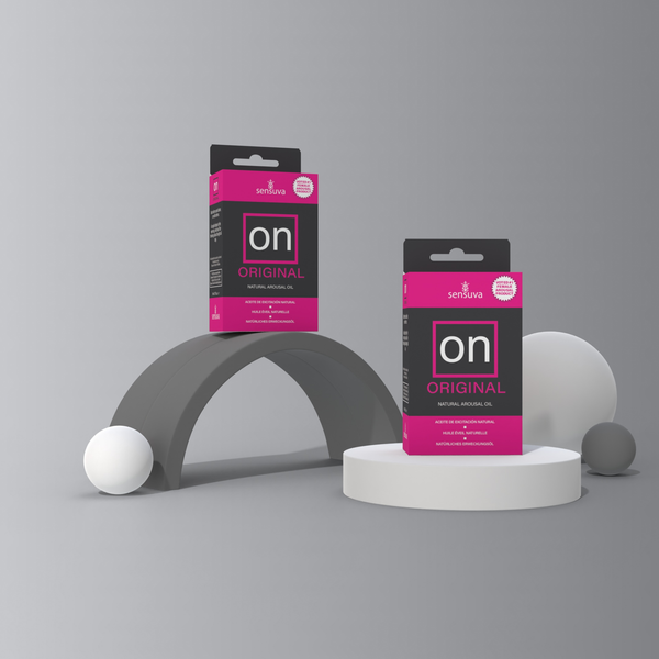 Two boxes of Sensuva ON Original Natural Arousal Oil are artfully displayed on grey and white geometric pedestals. Solid white and grey spheres surround the layout against a matching minimalist grey backdrop.