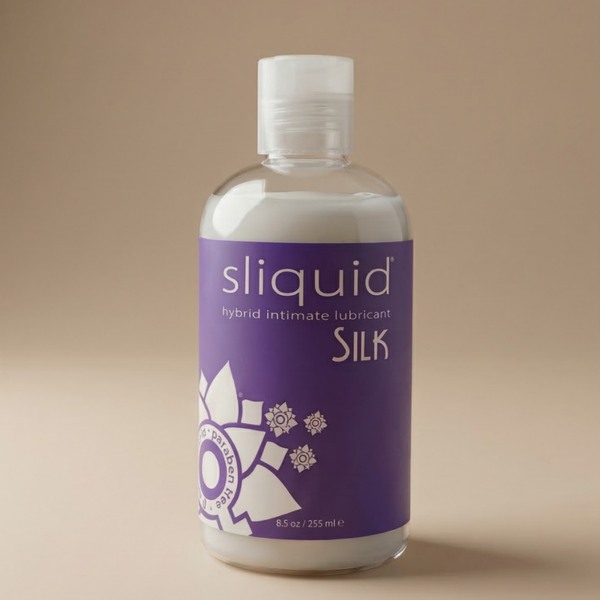 Upright studio product view of the 8.5 oz (255 ml) clear bottle filled with opaque white Sliquid Silk hybrid intimate lubricant, featuring a deep purple label and clear disc cap against a warm beige background.