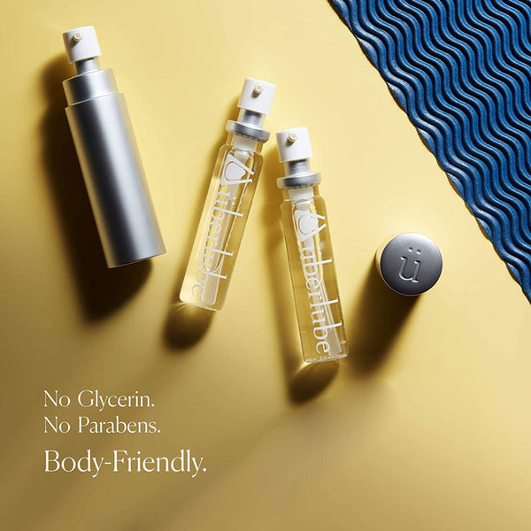 Three bottles of Uberlube, one silver and two clear, are arranged on a yellow surface next to a textured blue mat. The image emphasizes that the product, sold by Worldcondoms, is "No Glycerin. No Parabens. Body-Friendly."