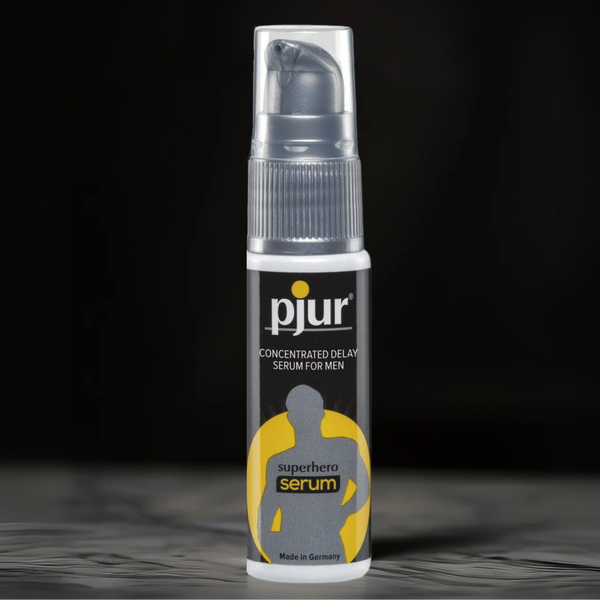 White and black Pjur Superhero Serum bottle with a yellow 'superhero serum' icon, set against a blurred dark background.