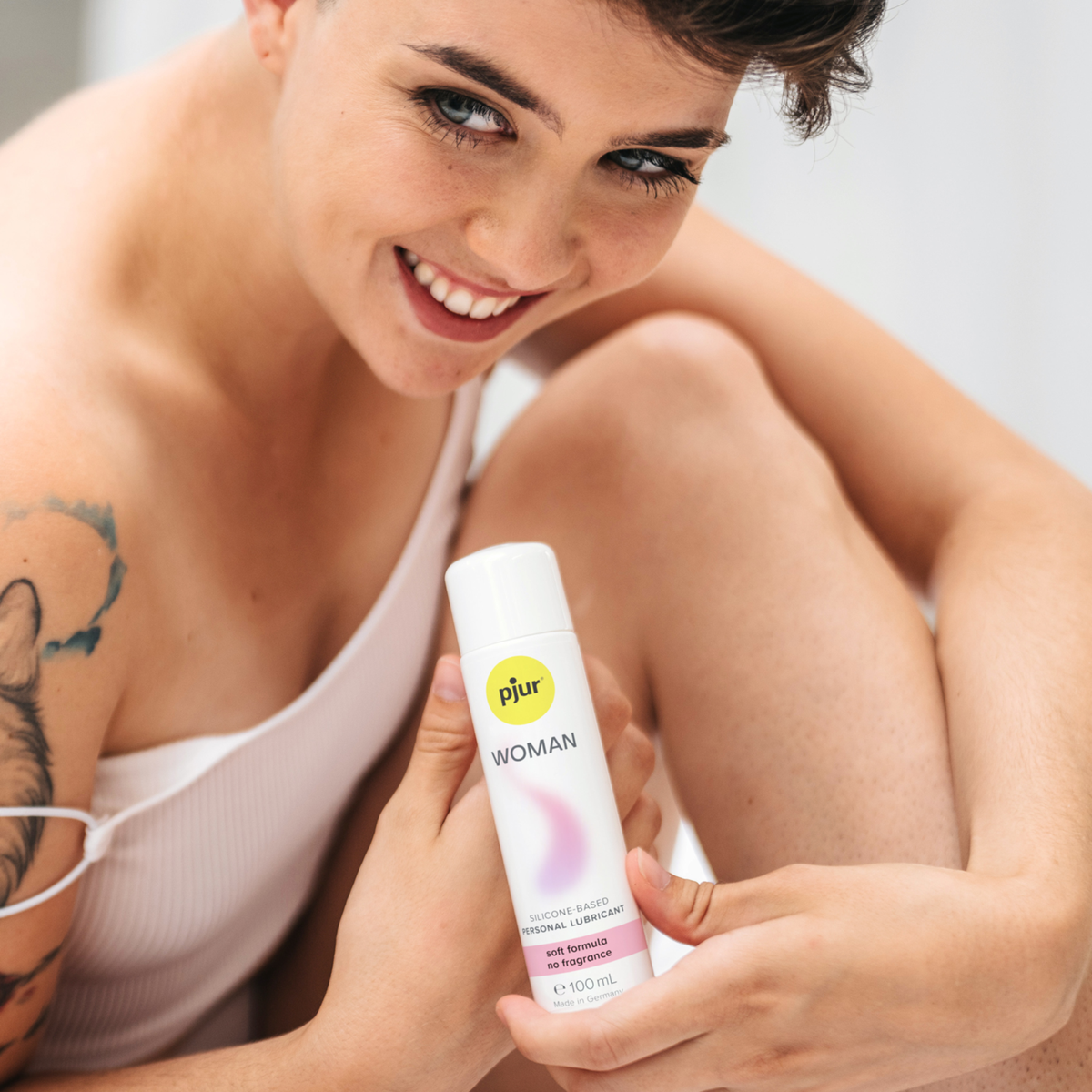 Smiling woman with short hair holding a bottle of pjur Woman Silicone-Based Personal Lubricant (soft formula, no fragrance).