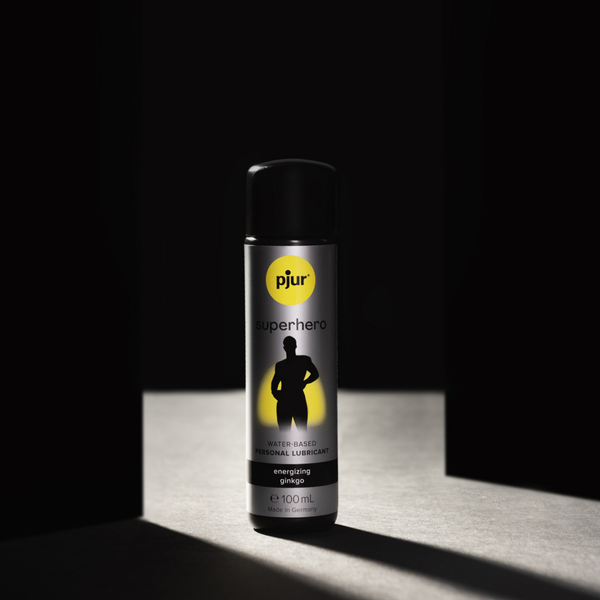 A gray bottle of Pjur Superhero lubricant stands on a surface with dramatic lighting against a dark background.
