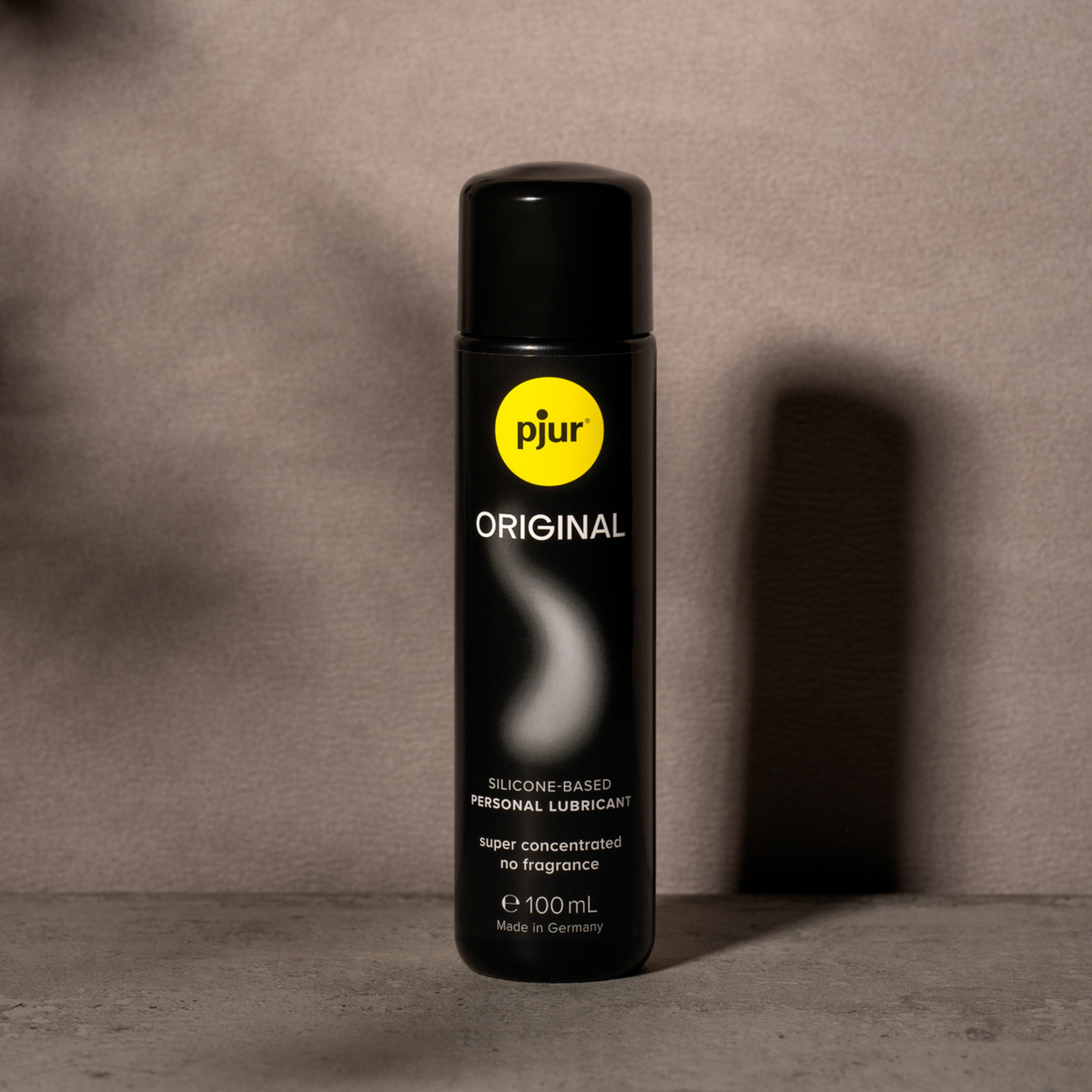 A black bottle of Pjur Original silicone-based personal lubricant is positioned against a neutral gray background.