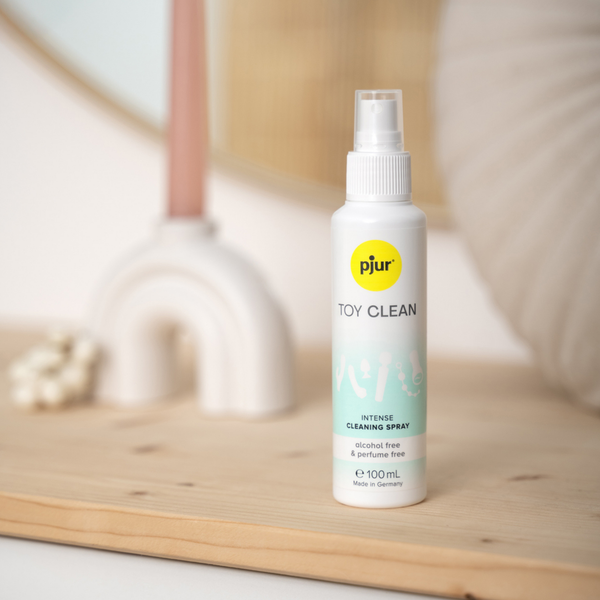 A white spray bottle of Pjur Toy Clean sits on a wooden surface.