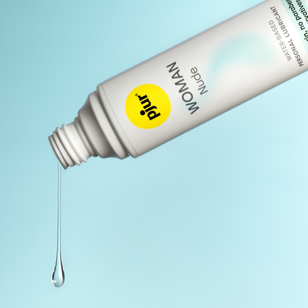 A droplet of clear pjur WOMAN Nude water-based personal lubricant falling from the tube against a light blue background.