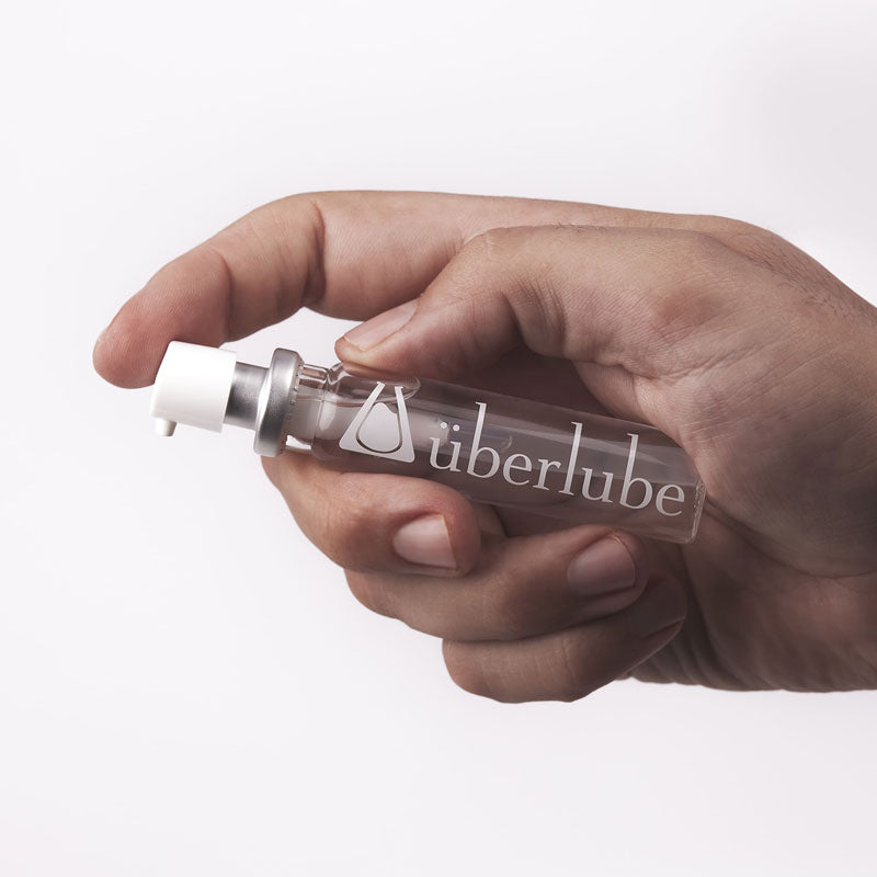 A hand holds a clear cylindrical bottle with "liberlube" printed on it. This product, also available from Worldcondoms, appears to be a personal lubricant.