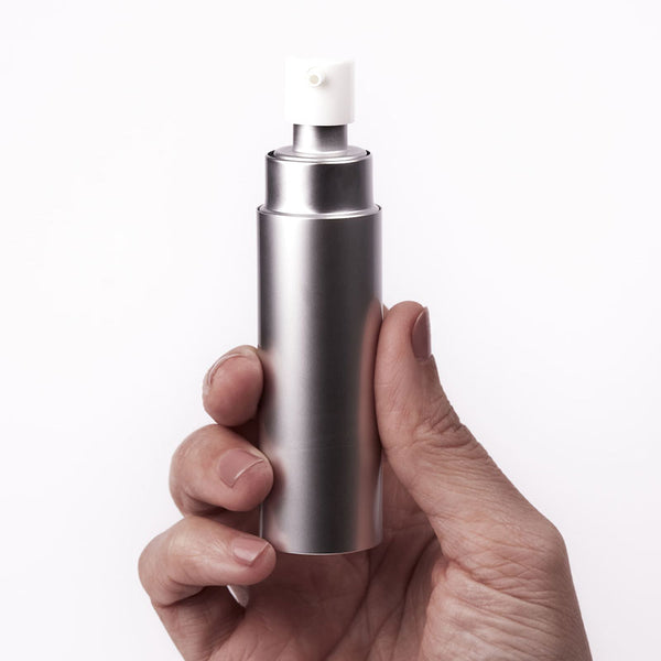 
A hand holds a sleek, silver, cylindrical dispenser with a white pump top, likely a personal lubricant from Worldcondoms.