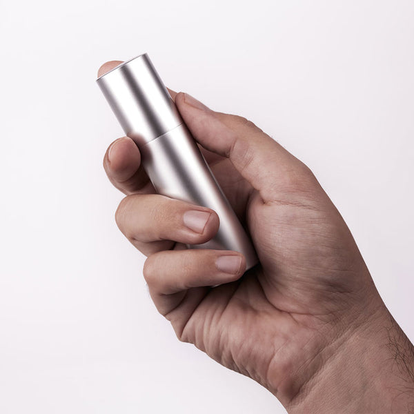 A hand holds a sleek, silver, cylindrical dispenser with a white pump top, likely a personal lubricant from Worldcondoms.
