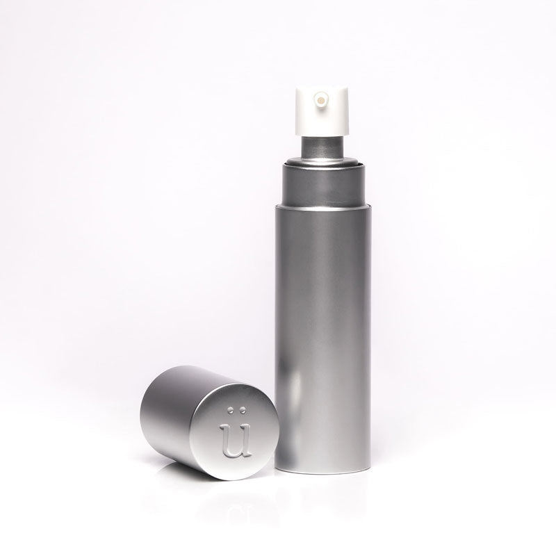 A clear "überlube" bottle with a white pump top stands  featuring the "ü" logo on its end, both products available from Worldcondoms.